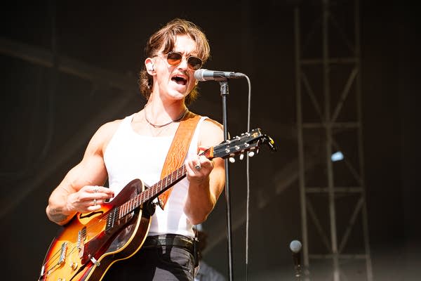 A musician sings and plays guitar on an outdoor stage