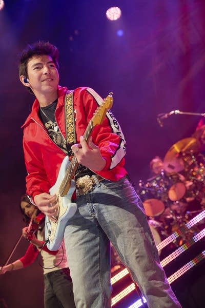 A musician plays guitar onstage in a large music venue