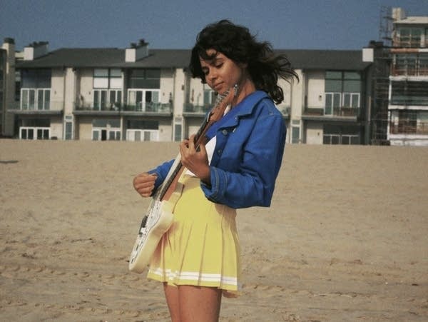 Natasha Janfaza plays electric guitar on a beach.
