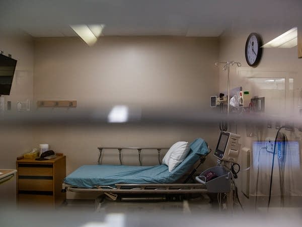 A hospital bed sits behind a curtained window. 