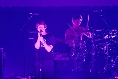 A man singing while another man plays drums on stage in a large arena