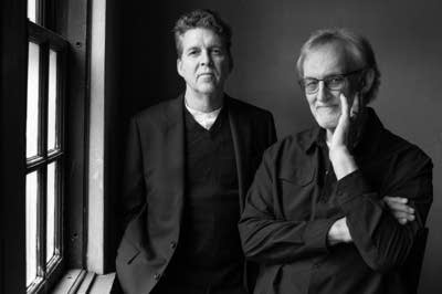 Two men stand next to a window for a portrait