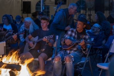 a crowd of people playing music around a campfire 
