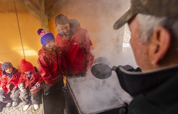 Students look on as a man creates maple syrup