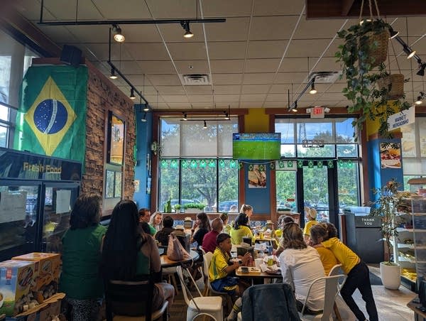 Fans gather in a cafe to watch a soccer match. There's a Brazil flag hanging up to the left.